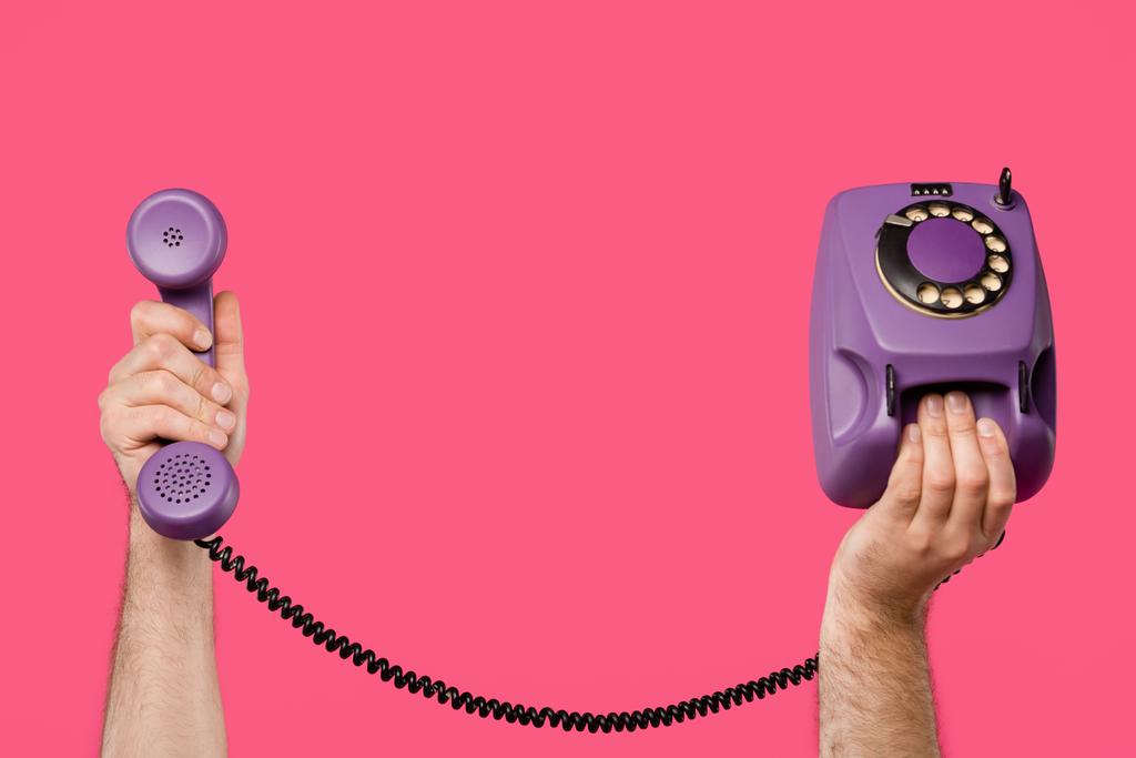 περικοπεί shot του ανθρώπου που κρατώντας μωβ περιστροφικό τηλέφωνο που απομονώνονται σε ροζ - Φωτογραφία, εικόνα