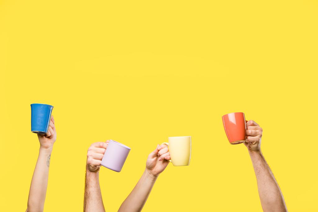 黄色の分離されたカラフルなカップを保持している男性と女性の手のショットをトリミング - 写真・画像