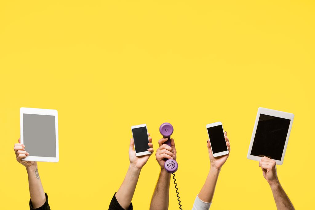 recortado tiro de manos sosteniendo teléfonos inteligentes, tabletas digitales y auriculares aislados en amarillo
  - Foto, imagen