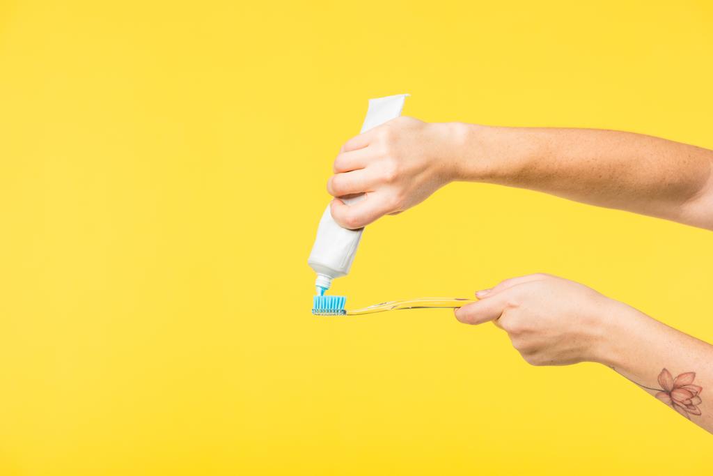 tiro recortado de la persona sosteniendo cepillo de dientes y pasta de dientes aislados en amarillo
 - Foto, Imagen