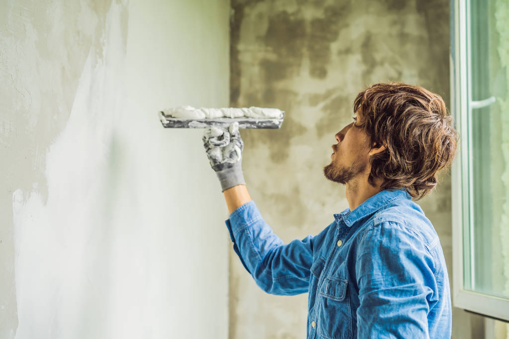 Trabalhador masculino aplicando massa branca na parede e manchando por faca de vidraceiro
. - Foto, Imagem