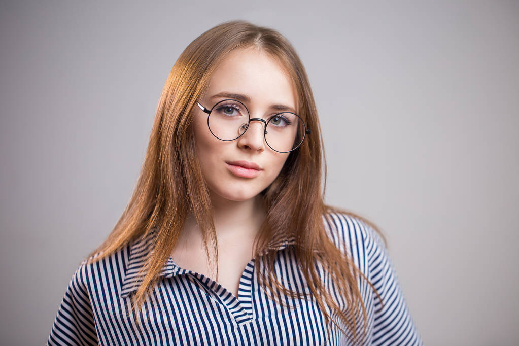 Horizontale portret van mooie jonge vrouw die het dragen van bril en shirt op grijze achtergrond met kopie ruimte. Student meisje camera kijken - Foto, afbeelding