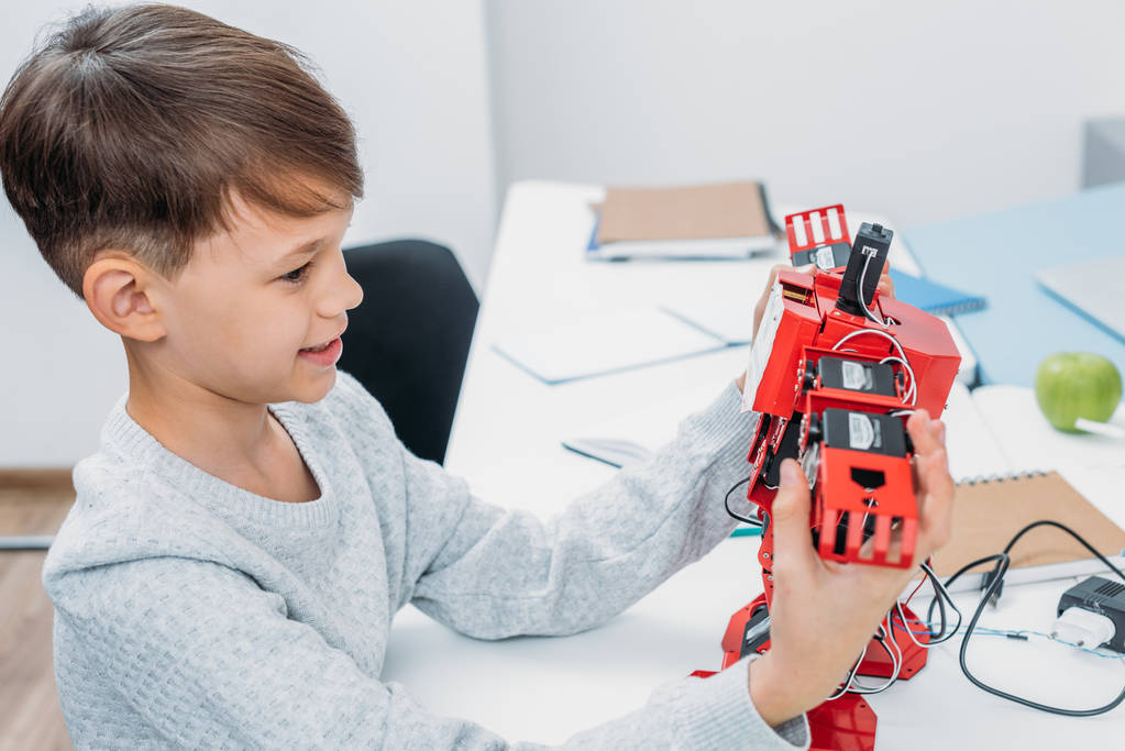 écolier souriant tenant robot rouge fabriqué avec des blocs de construction en plastique dans la classe de tige
 - Photo, image