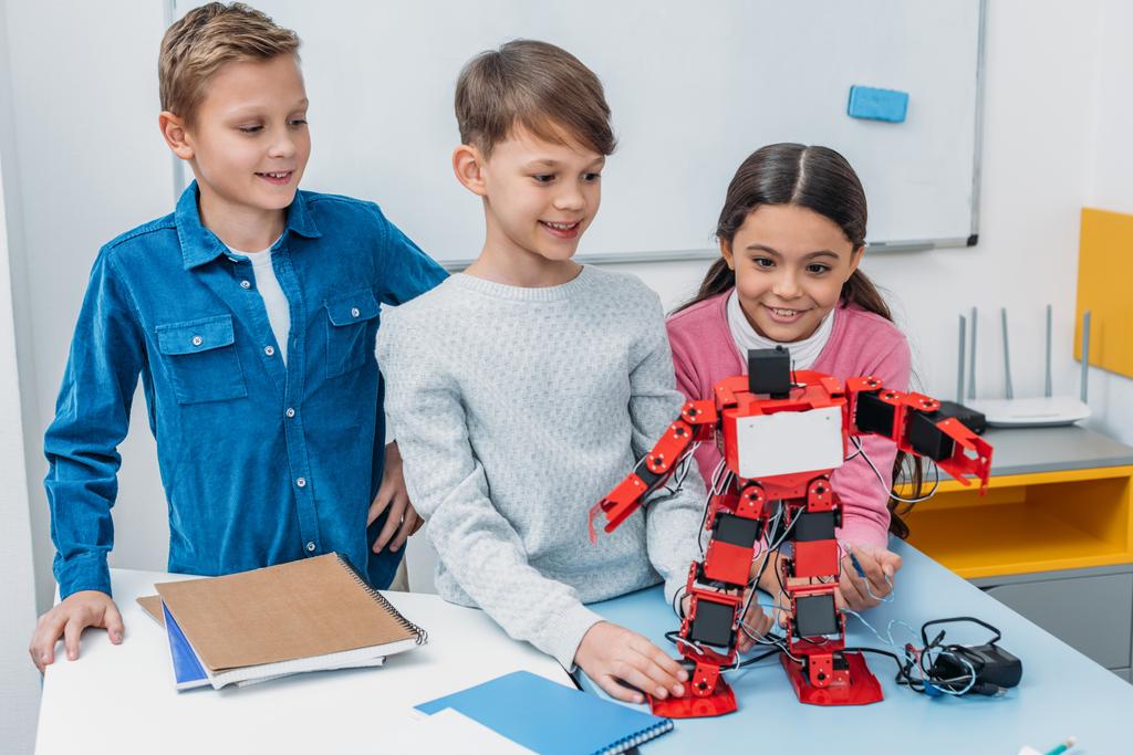 happy schoolchildren touching red handmade robot at desk in stem class - Photo, Image