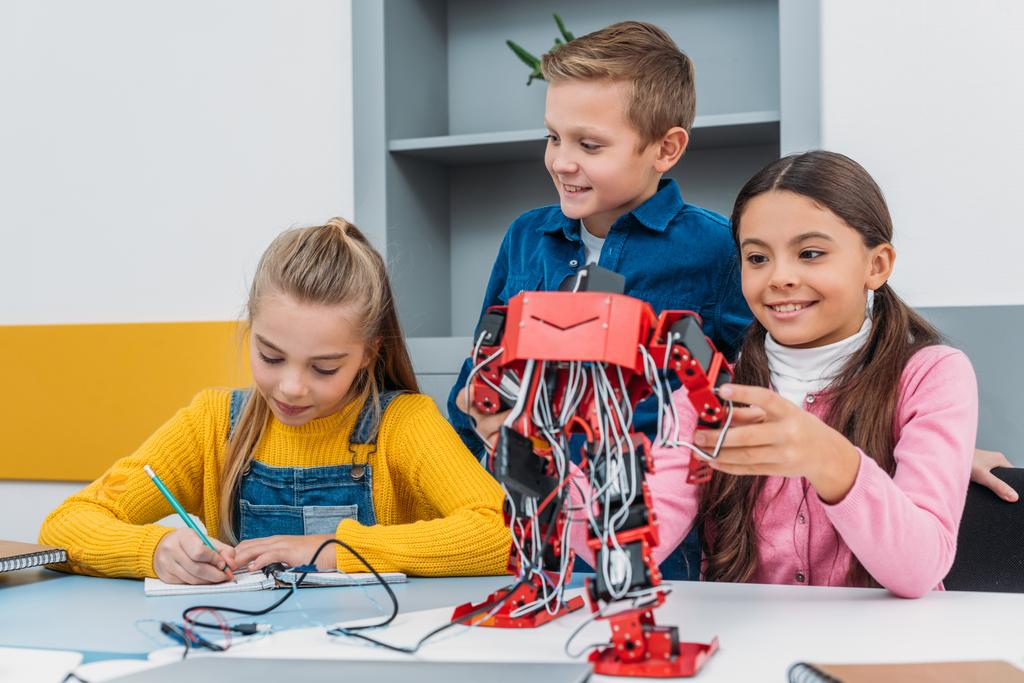 glimlachend schoolkinderen maken rode robot in stam education klasse - Foto, afbeelding