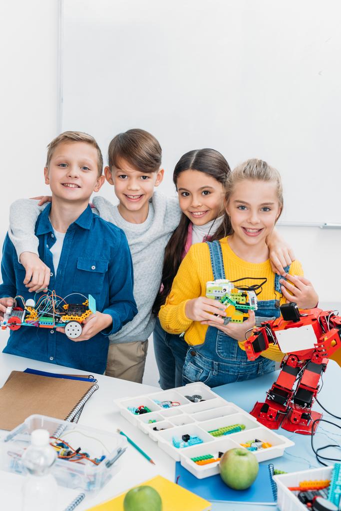happy schoolchildren looking at camera and holding handmade robots in stem class - Photo, Image