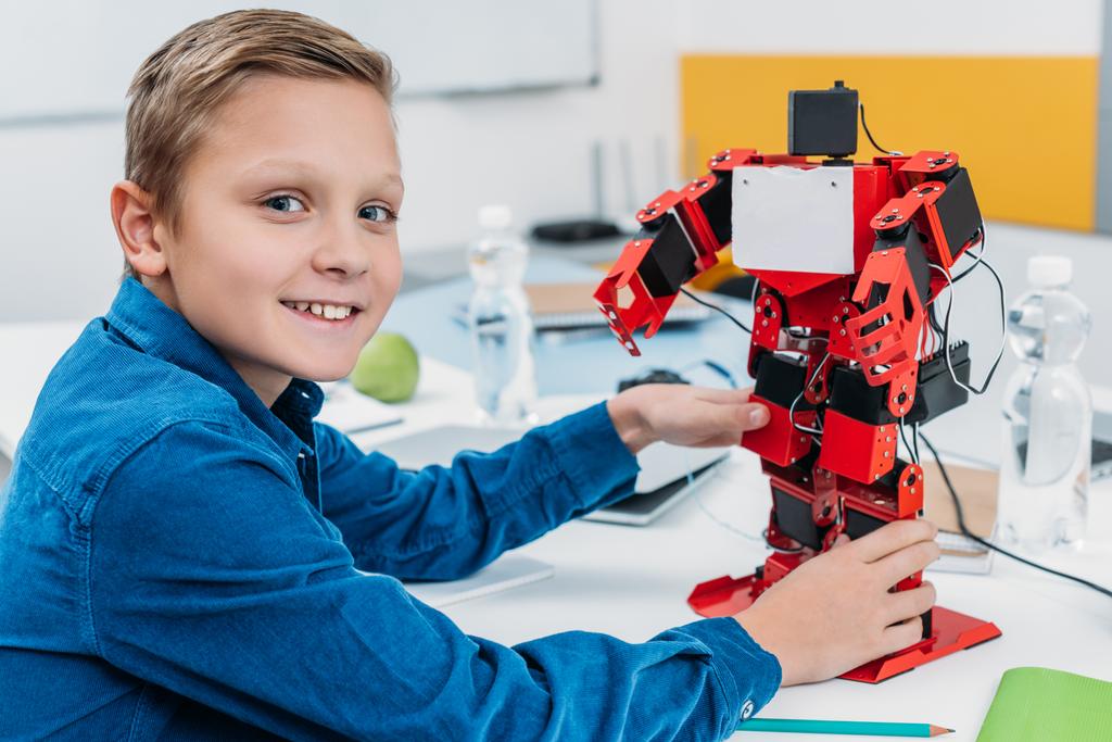 menino sorrindo segurando robô elétrico vermelho e olhando para a câmera durante a lição de tronco
 - Foto, Imagem