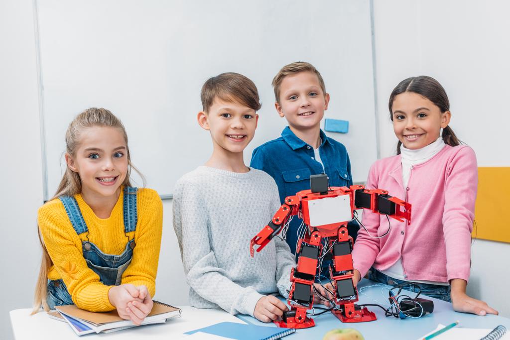 Glückliche Schulkinder stehen mit rotem Elektroroboter in der Klasse am Schreibtisch - Foto, Bild