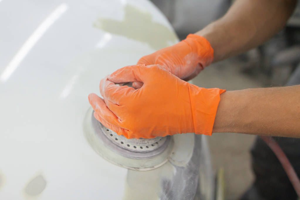 men's hands in orange gloves polish the hood of a car with a pneumatic polisher in the garage - Photo, Image