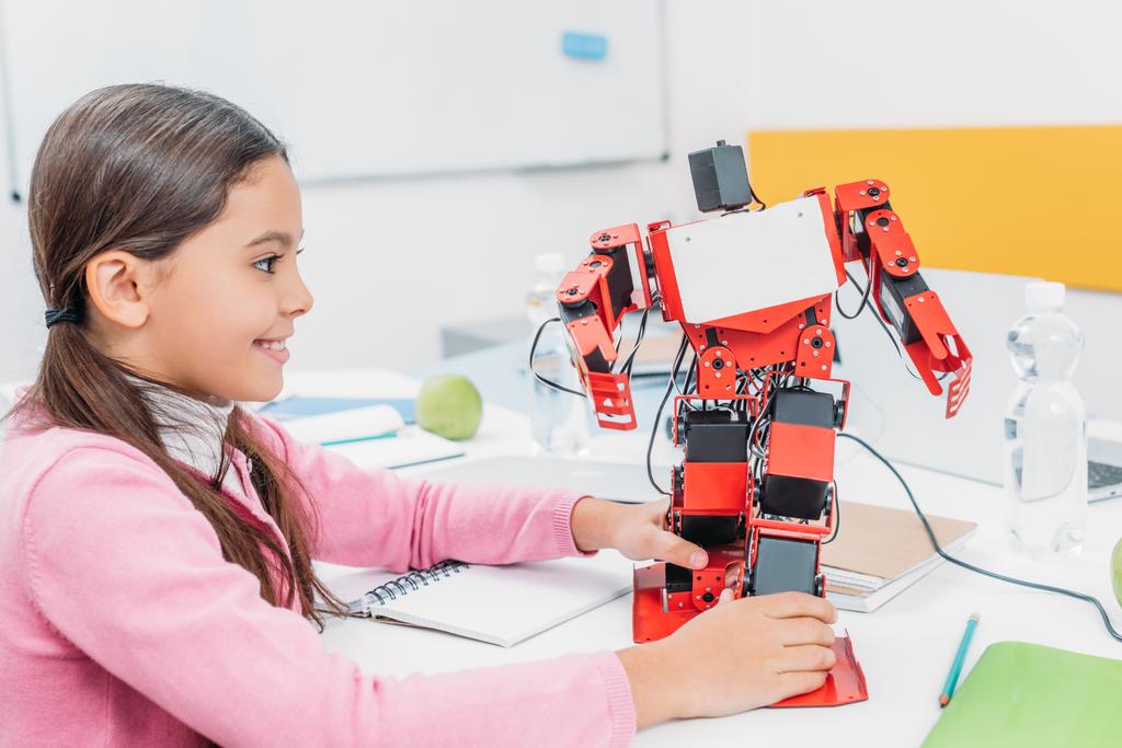 roztomilá školačka u stolu v kmenové učebně a hrát si s robotem modelu - Fotografie, Obrázek