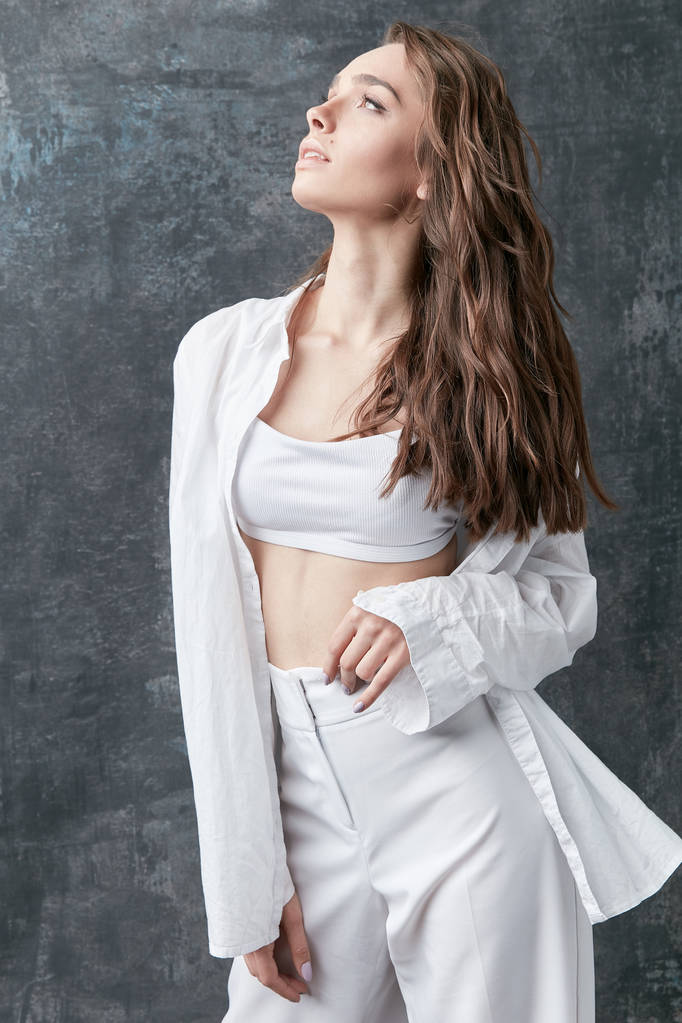 Moda tiro de bela mulher morena posando em camisa branca, top e calças. Estúdio, fundo cinza
 - Foto, Imagem