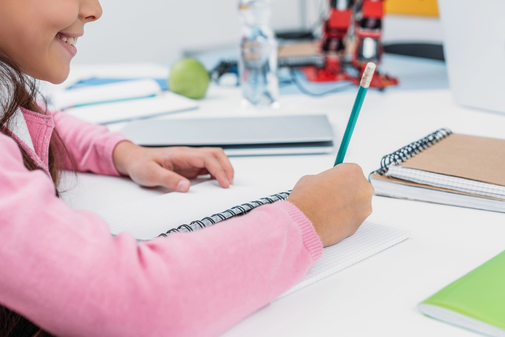 Ausgeschnittene Ansicht einer Schülerin am Schreibtisch, die während des Unterrichts im Klassenzimmer in ein Notizbuch schreibt - Foto, Bild