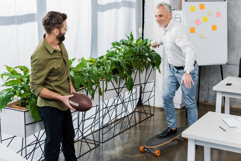 Lächelnde Geschäftsleute mit Skateboard und Rugbyball im Büro - Foto, Bild