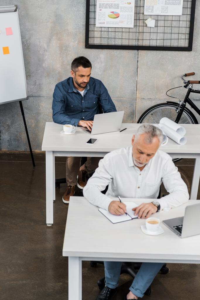 visão de alto ângulo de empresários sentados em mesas e trabalhando no escritório
 - Foto, Imagem