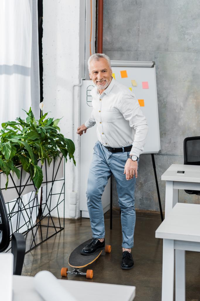 alegre guapo mediana edad empresario poner pierna en longboard en oficina
 - Foto, imagen