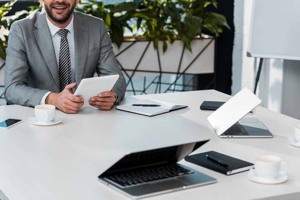 bijgesneden afbeelding van zakenman tablet houden aan tafel in kantoor - Foto, afbeelding