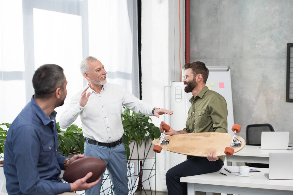 homens de negócios bonitos sorridentes se divertindo e conversando no escritório
 - Foto, Imagem