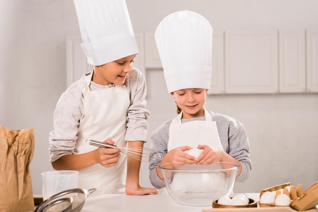 enfoque selectivo de los niños en delantales y sombreros de chef durante la preparación de alimentos en la mesa en la cocina
  - Foto, Imagen