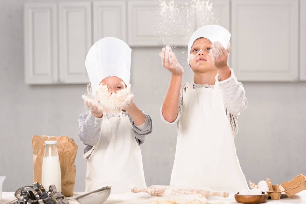 сестра і брат в капелюхах шеф-кухаря розважаються з борошном на кухні
  - Фото, зображення