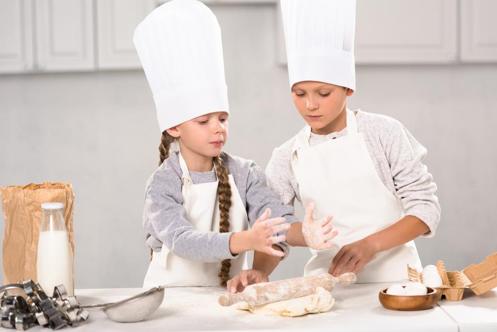 エプロンやキッチンのテーブルで麺棒で生地を作るシェフ帽子子供 - 写真・画像