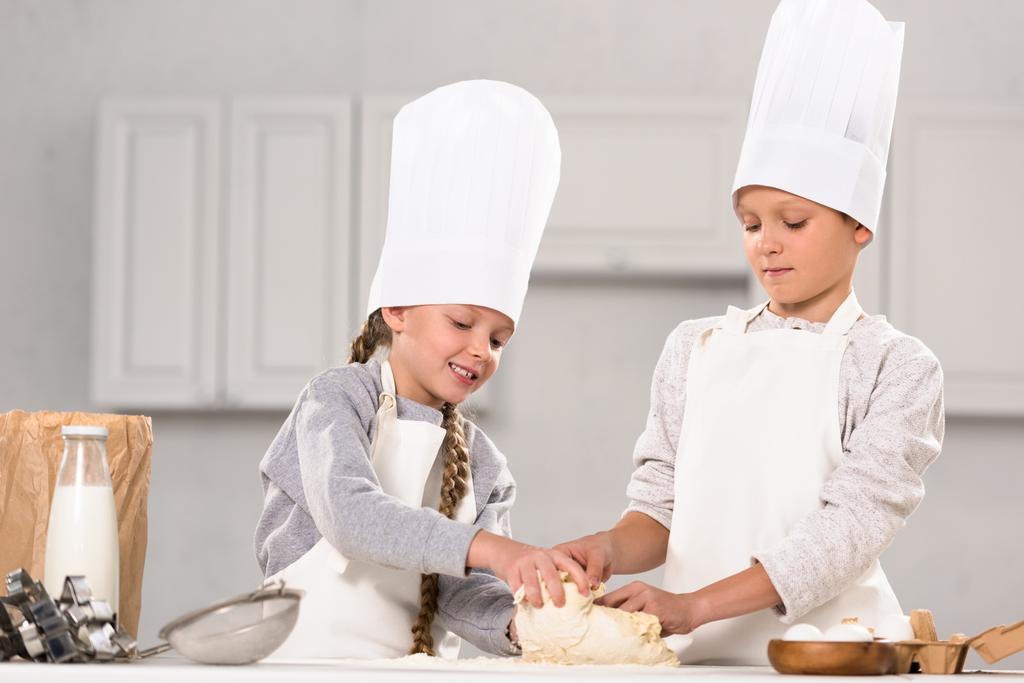 улыбающиеся брат и сестра готовят тесто для печенья за столом на кухне
 - Фото, изображение