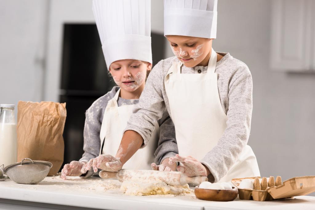Selektywny fokus dzieci w fartuchy i czapki szefa kuchni, Dokonywanie ciasta z wałkiem przy stole w kuchni - Zdjęcie, obraz