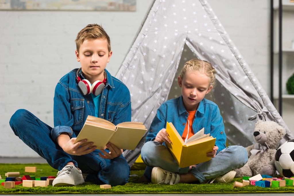 focada irmãzinha e irmão lendo livros perto da tenda em casa
 - Foto, Imagem