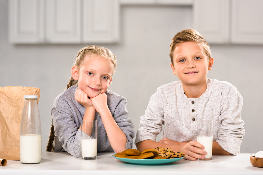 fratello felice e sorella guardando la fotocamera vicino al tavolo con latte e biscotti
 - Foto, immagini