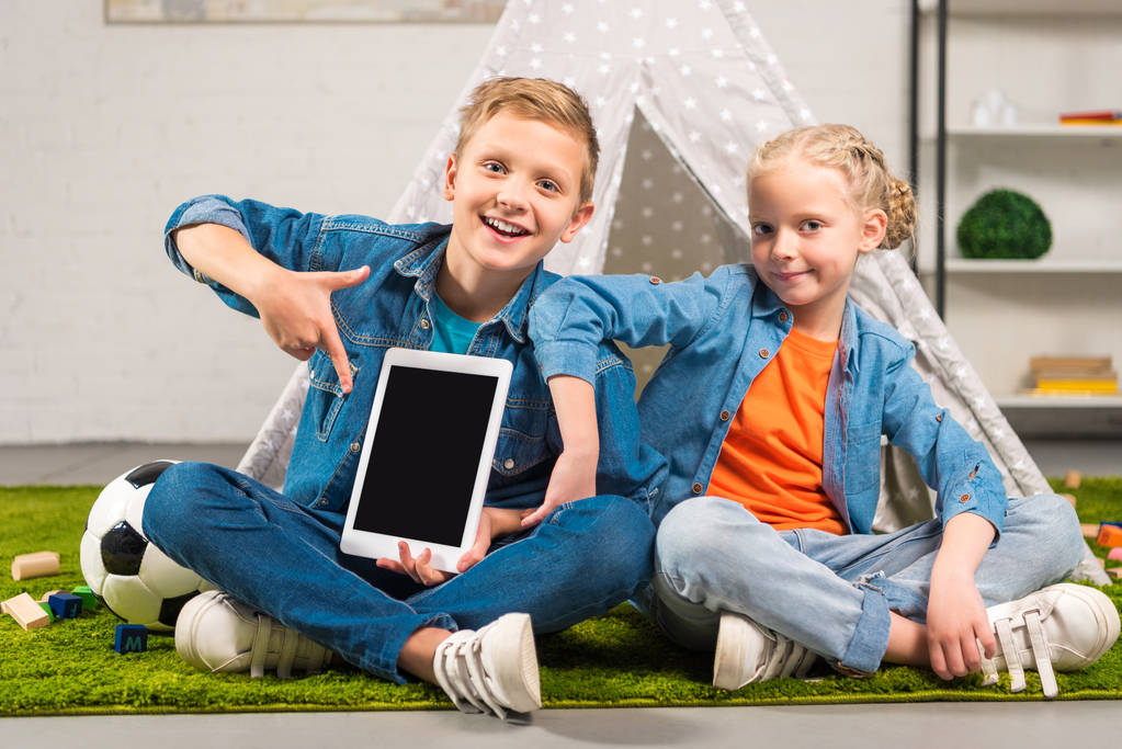 boy pointing at digital tablet with blank screen and his sister sitting near tent at home - Photo, Image