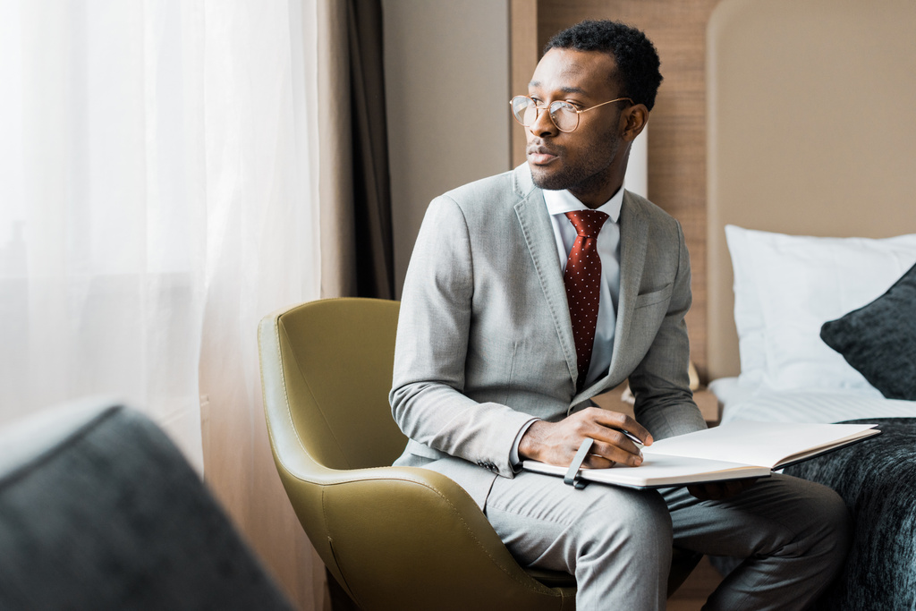 schöner afrikanisch-amerikanischer Geschäftsmann mit Tagebuch im Hotelzimmer - Foto, Bild