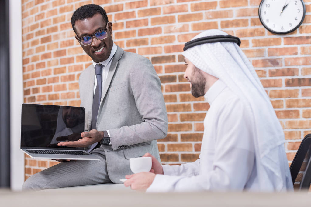 Afro-Amerikaanse zakenman tonen van laptop aan Arabische partner in kantoor  - Foto, afbeelding
