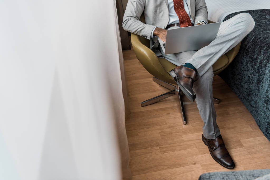 bijgesneden weergave van elegante zakenman met laptop in hotelkamer - Foto, afbeelding