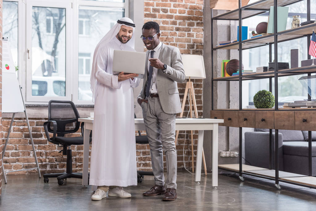 Des hommes d'affaires multiethniques debout avec ordinateur portable dans un bureau moderne
  - Photo, image