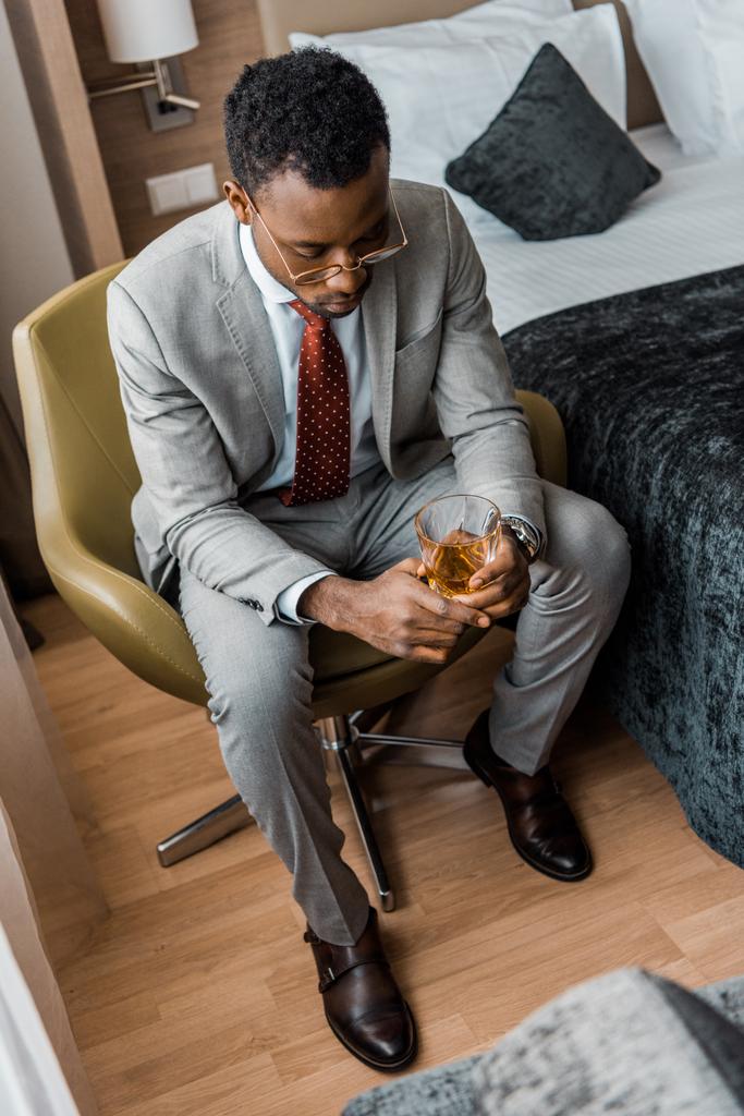 depressed african american man holding glass of whiskey in hotel room - Photo, Image