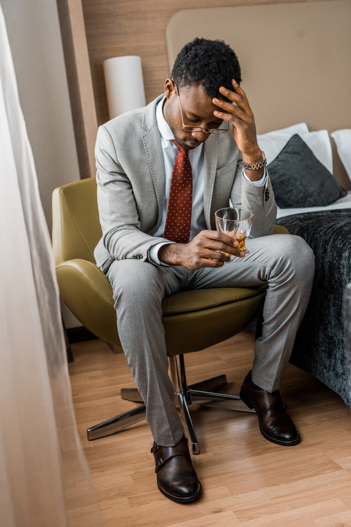 frustrato afroamericano uomo in possesso di vetro di cognac in camera d'albergo
 - Foto, immagini