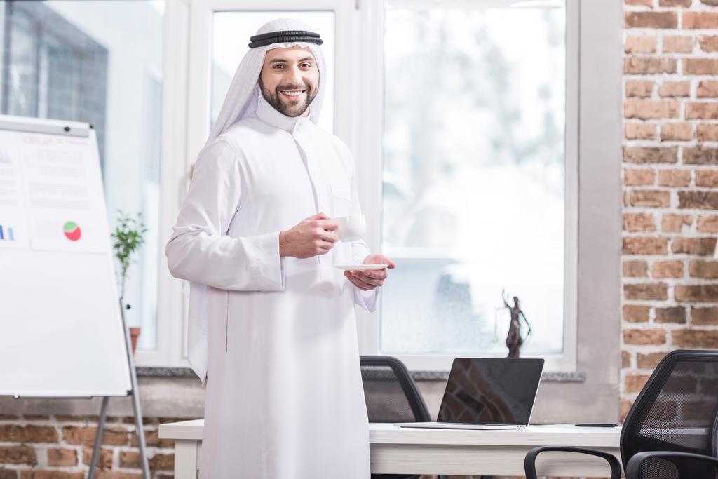 近代的なオフィスにドリンクを飲みながらカップを保持しているアラビア語の実業家  - 写真・画像