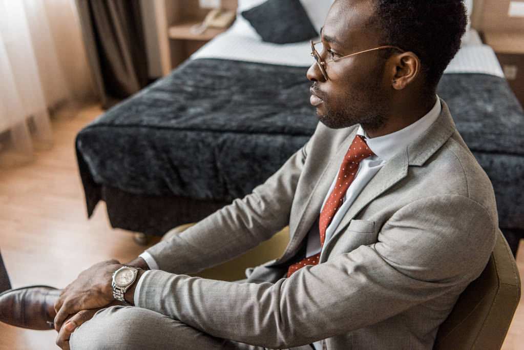 mietteliäs afrikkalainen amerikkalainen liikemies harmaassa puvussa istuu hotellihuoneessa
 - Valokuva, kuva