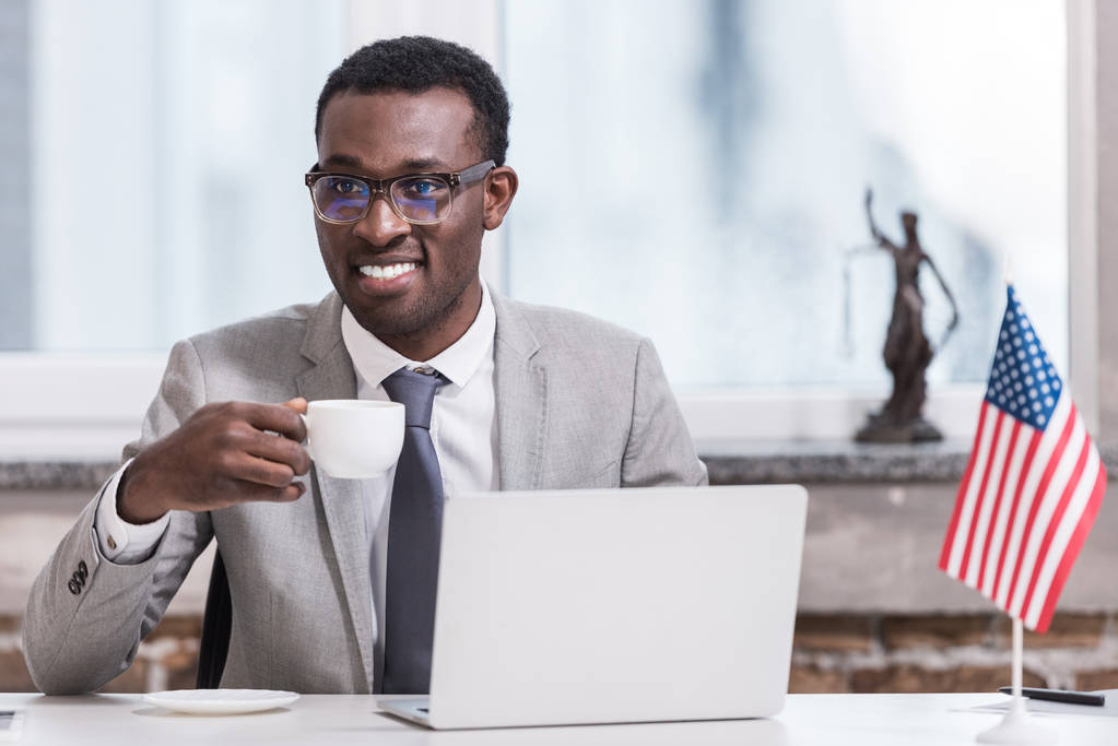 近代的なオフィスにドリンクを飲みながらカップを保持しているアフリカ系アメリカ人のビジネスマン  - 写真・画像