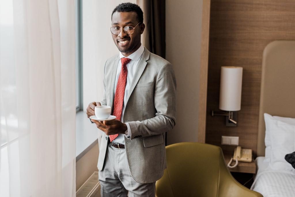 веселый африканский американский бизнесмен держит чашку кофе в гостиничном номере
 - Фото, изображение