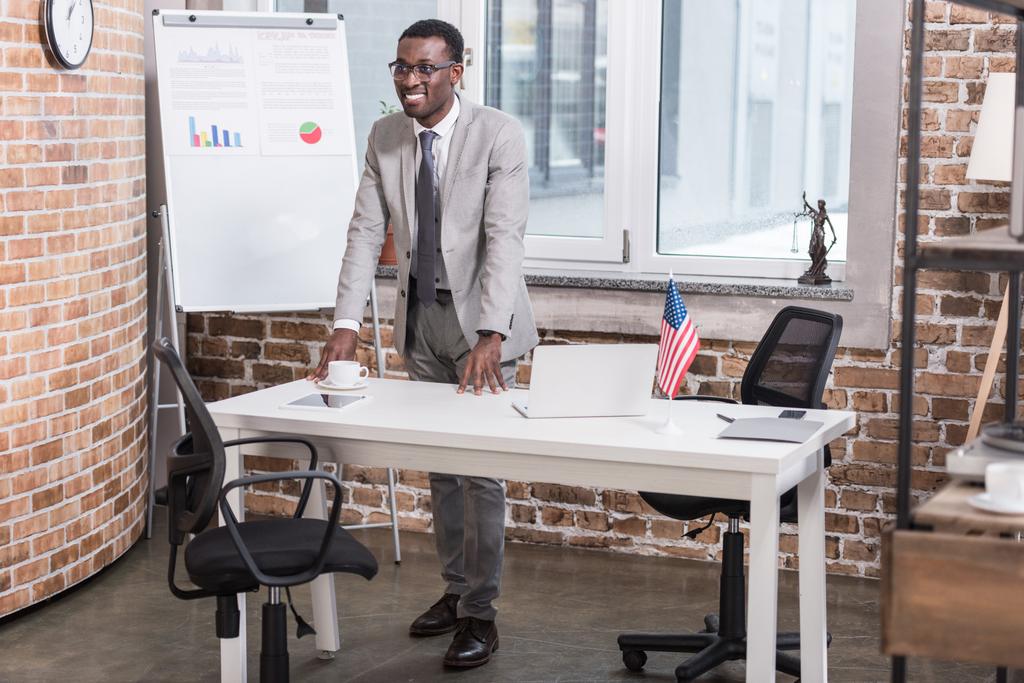 Африканский американский бизнесмен, стоящий за столом офиса
 - Фото, изображение