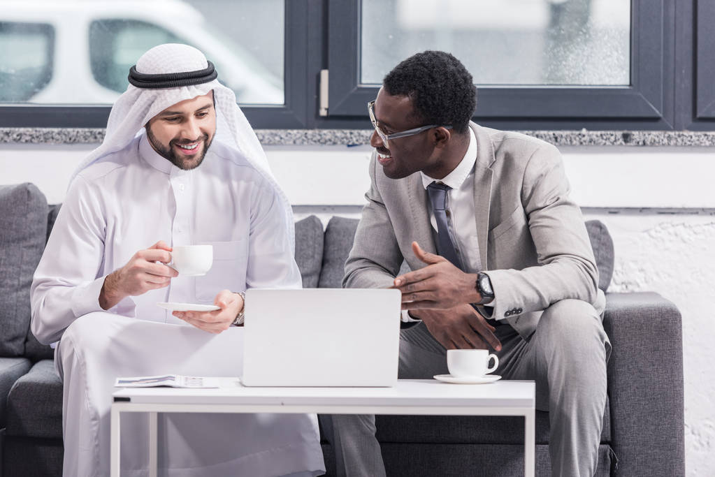Афро-американських бізнесмен, дивлячись на арабській партнера і посміхаючись в офісі  - Фото, зображення
