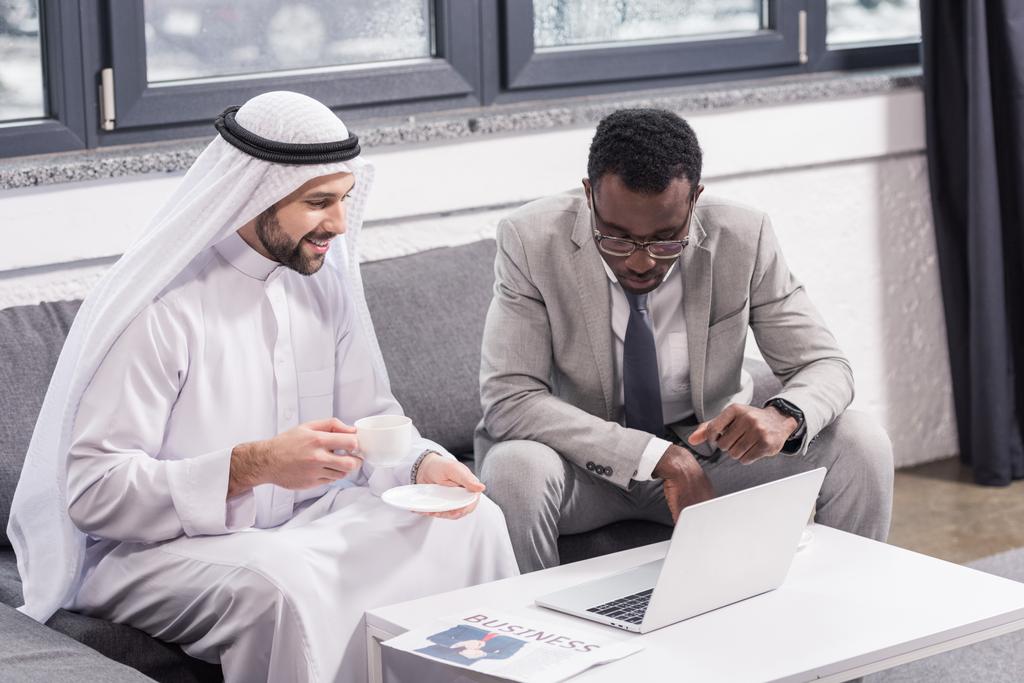 Des hommes d'affaires multiculturels assis et regardant un ordinateur portable dans un bureau moderne
  - Photo, image