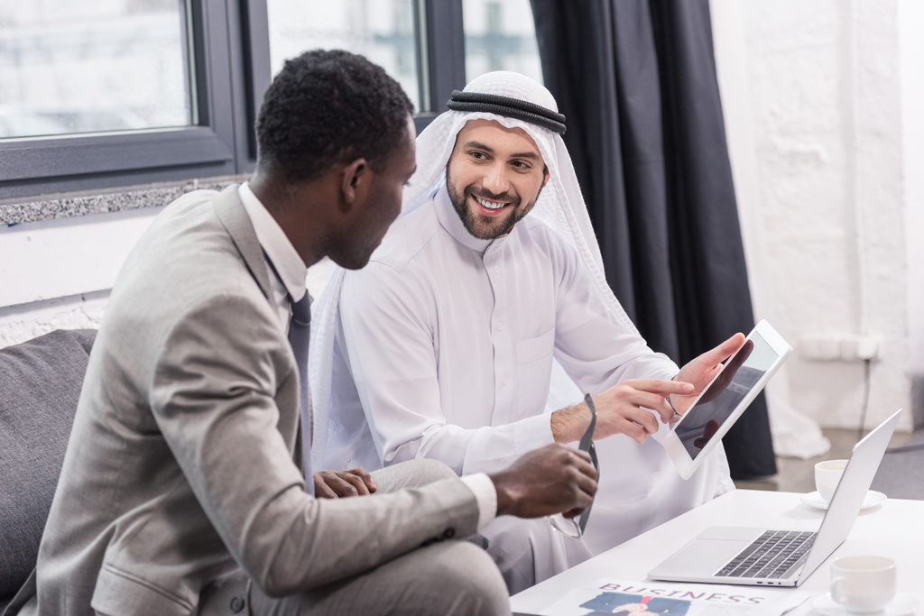 Arabo uomo d'affari sorridente e utilizzando il dispositivo digitale in ufficio moderno
 - Foto, immagini