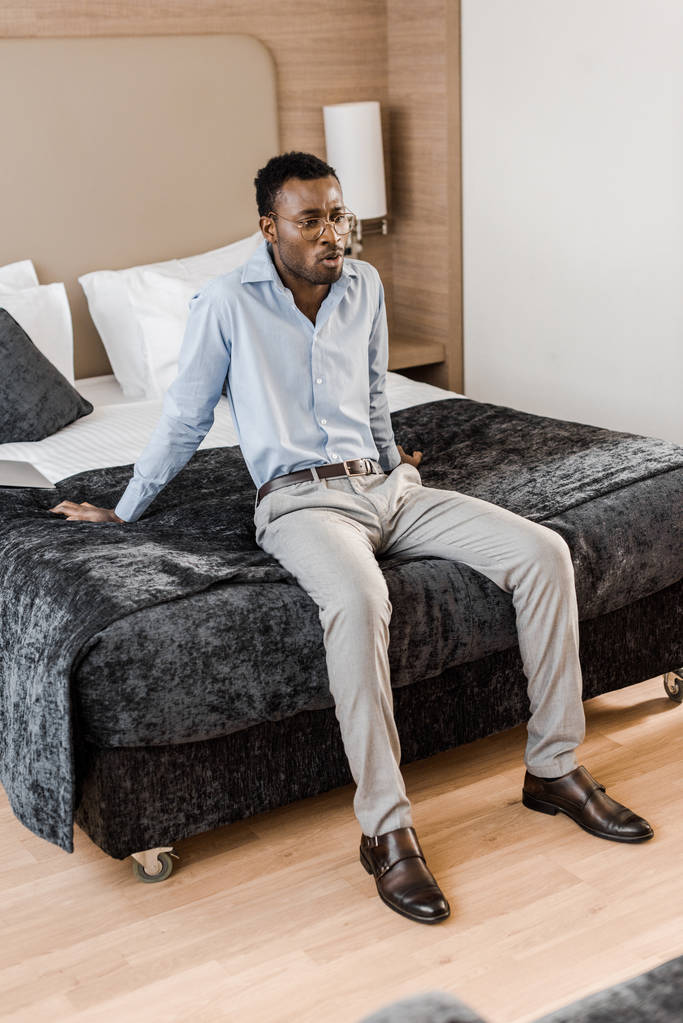 νεαρός αφρικανική αμερικανική άνθρωπος που κάθεται στο κρεβάτι στο δωμάτιο του ξενοδοχείου - Φωτογραφία, εικόνα