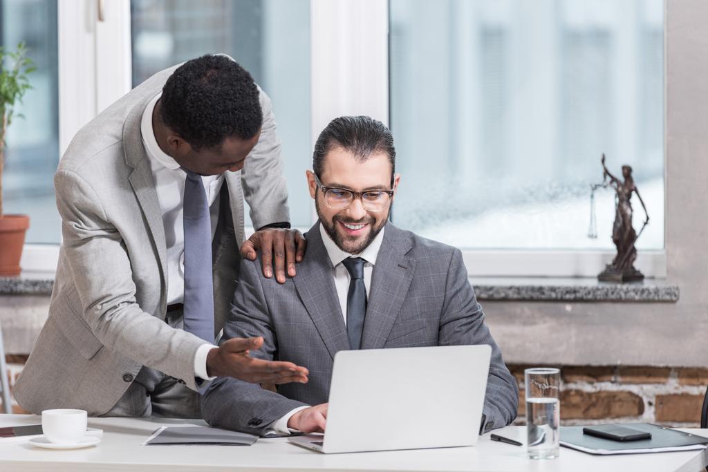 hombre de negocios afroamericano poniendo la mano en los socios hombro y apuntando a la computadora portátil en la oficina
 - Foto, Imagen