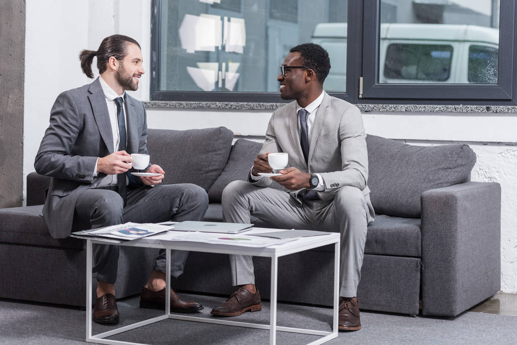 Multiethnische Geschäftsleute sitzen auf der Couch und trinken Kaffee im Büro - Foto, Bild