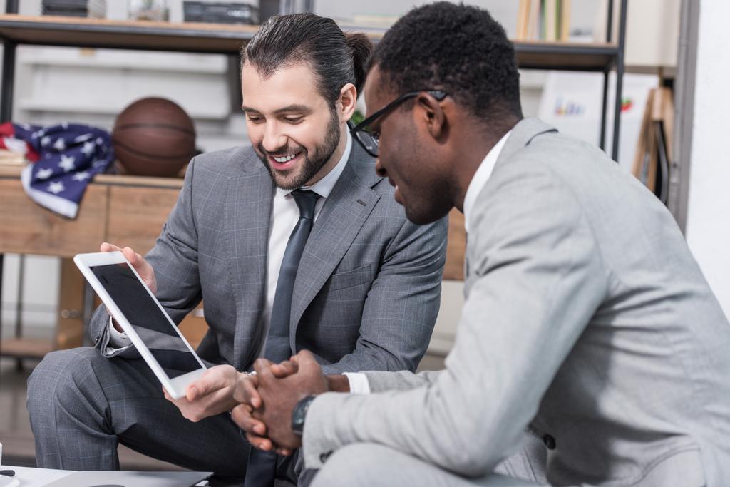 красивый бизнесмен показывает экран цифрового планшета африканскому деловому партнеру в офисе
 - Фото, изображение