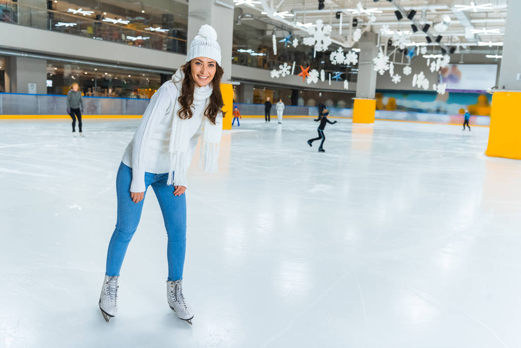Lächelnde junge attraktive Frau im Strickpullover läuft allein auf der Eisbahn Schlittschuh - Foto, Bild