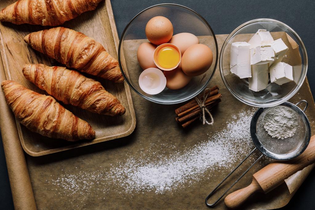 vista superior de papel manteiga coberto de farinha, croissants e ingredientes na mesa
 - Foto, Imagem