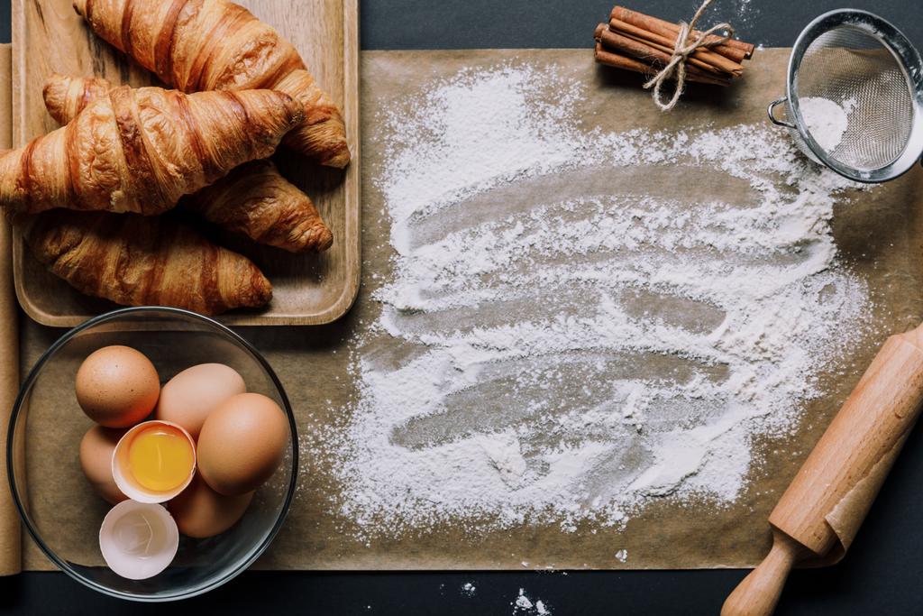 vista de cima de assar papel coberto de farinha, croissants e ovos na tigela na mesa
 - Foto, Imagem